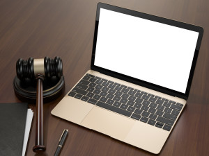 A gavel sits near a laptop and a pen and legal notebook